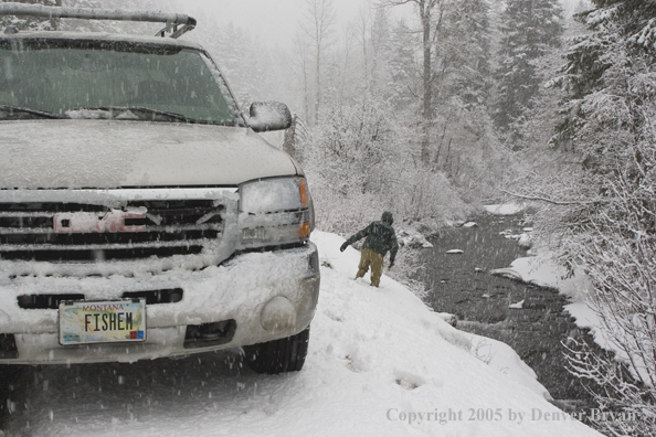 Flyfisherman climbing down snowy bank.  Truck in foreground.