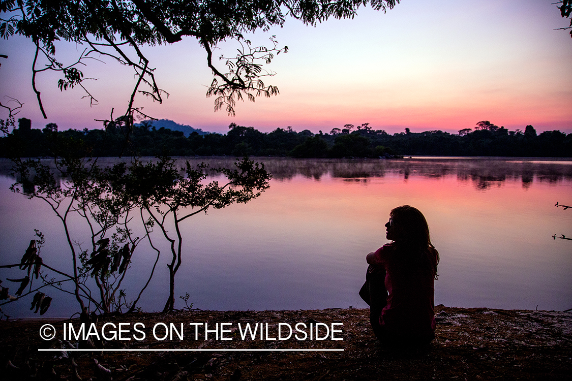 Woman sitting by river at sunset in Kendjam region, Brazil.