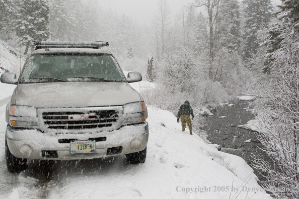 Flyfisherman climbing down snowy bank.  Truck in foreground.