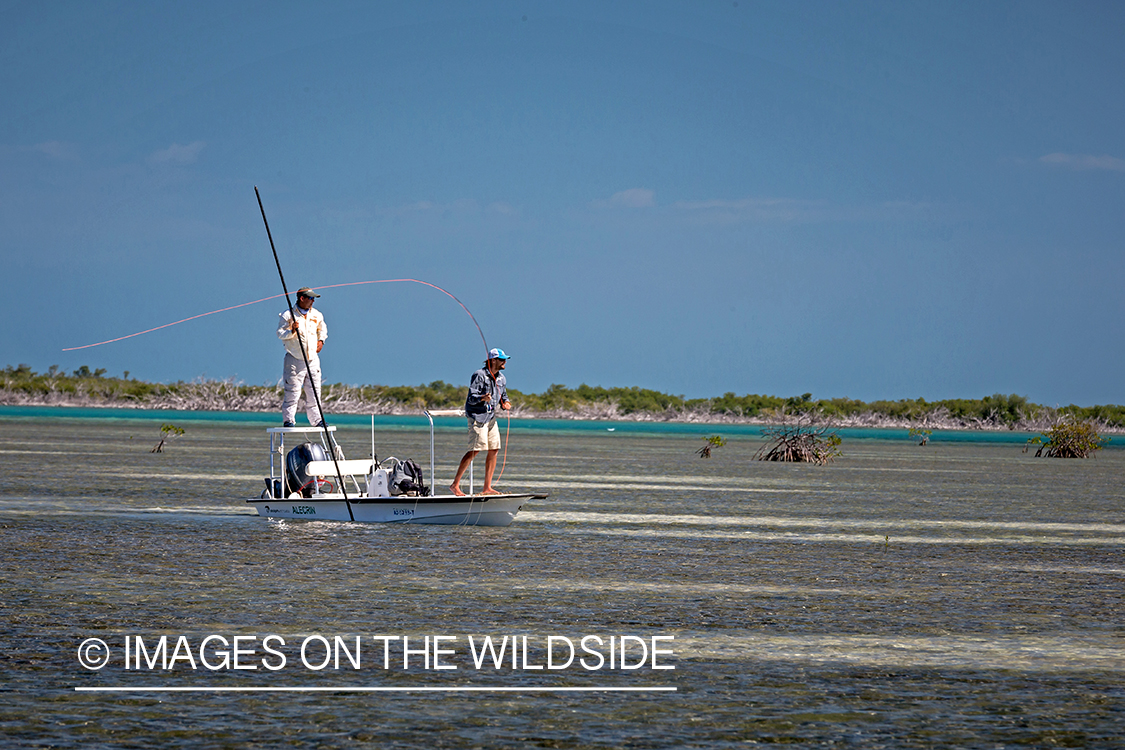 Flyfisherman casting line on flats boat with guide.