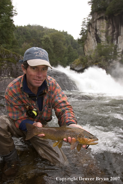 Flyfisherman holding brown trout.  Waterfall in background.