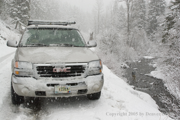 Flyfisherman on creek in snow storm.  Truck in foreground.