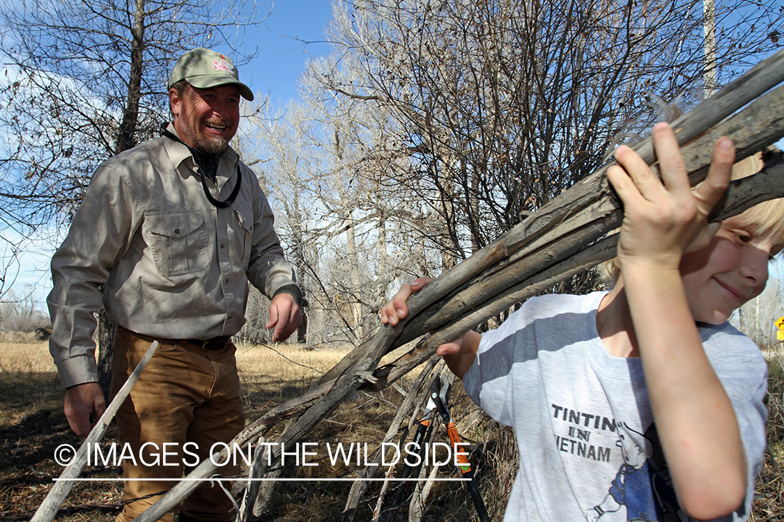 Father and son waterfowl hunters building blind.