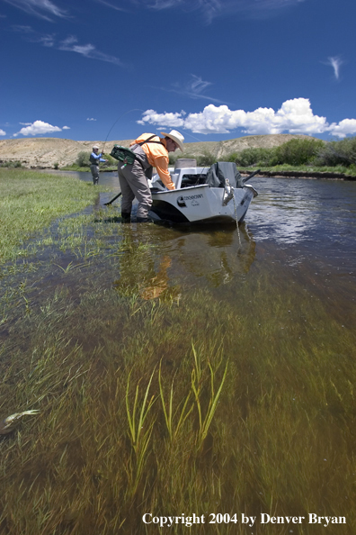 Flyfishermen fishing river (drift boat in foreground).  Summer.